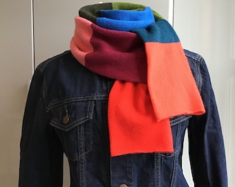May include: A colorful scarf with stripes of green, blue, burgundy, and orange. The scarf is folded and draped over a denim jacket.