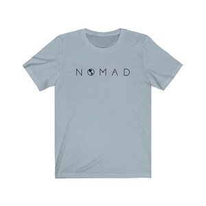 Puede incluir: Una camiseta azul claro con la palabra "NOMAD" impresa en letras negras. La "O" de "NOMAD" est&aacute; reemplazada por un peque&ntilde;o gr&aacute;fico de globo terr&aacute;queo negro.