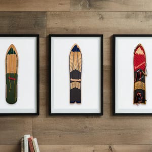 May include: Three framed vintage snowshoes displayed on a wooden wall. Each snowshoe has a unique design, with colors including natural wood, green, black, and red. The frames are black, and the background is white.