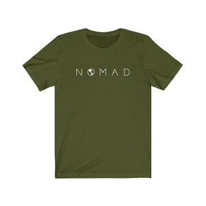 Puede incluir: Una camiseta verde de manga corta con la palabra "NOMAD" impresa en blanco en la parte delantera. La palabra "NOMAD" tiene un peque&ntilde;o icono de globo terr&aacute;queo en lugar de la letra "O".