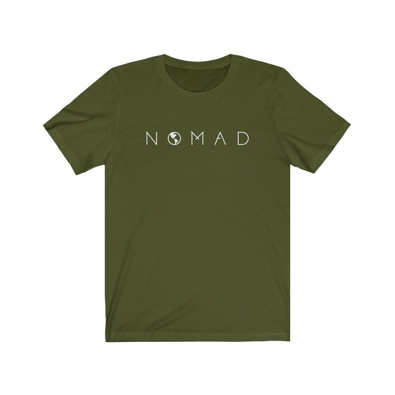 Puede incluir: Una camiseta verde de manga corta con la palabra "NOMAD" impresa en blanco en la parte delantera. La palabra "NOMAD" tiene un peque&ntilde;o icono de globo terr&aacute;queo en lugar de la letra "O".