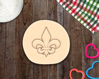 Könnte beinhalten: Nahaufnahme eines braunen Ausstechers in Form einer Fleur-de-lis, einer stilisierten Lilienblüte. Der Ausstecher liegt auf einer Holzoberfläche.