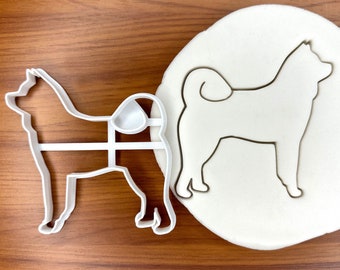 May include: White plastic cookie cutter in the shape of a Shiba Inu dog. The cutter is shown on a wooden surface with a sample of the cut-out shape on a white surface.