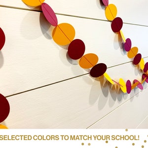 May include: A garland made of paper circles in yellow and burgundy. The garland is hanging on a white wood wall. The text "TWO SELECTED COLORS TO MATCH YOUR SCHOOL!" is at the bottom of the image.