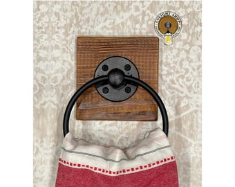 May include: A rustic wooden towel ring with a black metal ring and a black metal flange. The ring is mounted on a wooden board with a natural wood finish. A red and white striped towel is hanging on the ring.