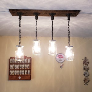 May include: A rustic farmhouse style chandelier with five glass jars hanging from a wooden beam. The jars have light bulbs inside and are wired with black chains.
