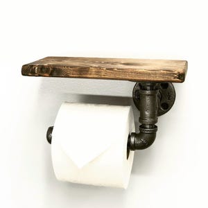 May include: A rustic wooden shelf with a black metal pipe toilet paper holder. The shelf is stained a dark brown color and the pipe is a matte black finish.