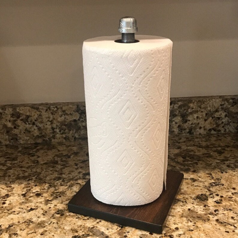 Puede incluir: Un soporte de papel de cocina de madera marr&oacute;n con una parte superior de metal plateado. Un rollo de papel de cocina blanco est&aacute; en el soporte.