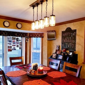 May include: A rustic-style light fixture with three clear glass jar pendant lights suspended from a dark wooden beam. The fixture is mounted above a bathroom vanity with a mirror and sink.