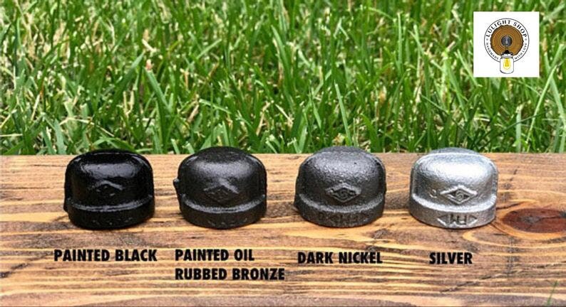 May include: Four metal pipe caps in different finishes: painted black, painted oil rubbed bronze, dark nickel, and silver. The caps have a diamond-shaped design.