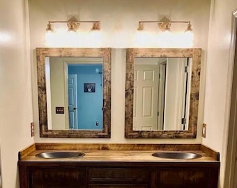 May include: A double bathroom vanity featuring a dark stained wood cabinet and countertop with two integrated oval sinks. Two rectangular mirrors with matching dark wood frames are mounted above, illuminated by two three-light wall fixtures.