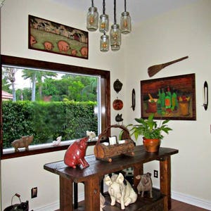 May include: A rustic, wooden cart with decorative pig figurines and a hanging light fixture made of mason jars. The room features artwork, a window with a view, and a potted plant.