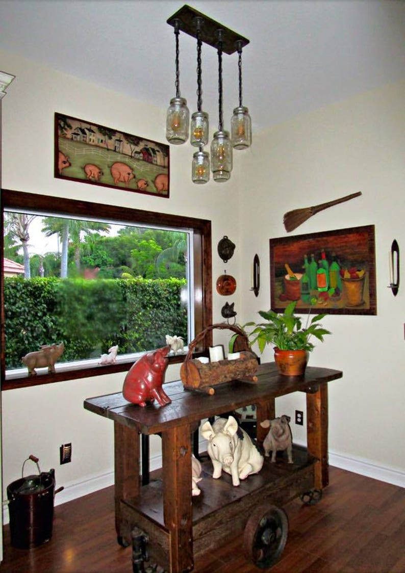 May include: A rustic, wooden cart with decorative pig figurines and a hanging light fixture made of mason jars. The room features artwork, a window with a view, and a potted plant.