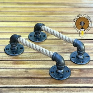 May include: Two black metal rope door pulls with a natural rope handle. The pulls are mounted on a wooden surface.