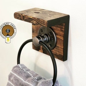 May include: A rustic wooden towel rack with a black metal ring and a shelf. The rack is mounted to a white wall. The towel rack is handmade with love.