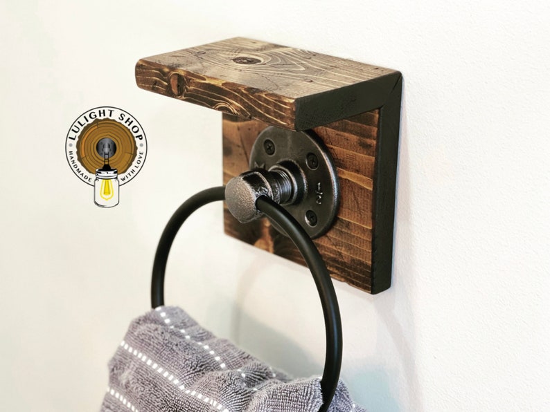 May include: A rustic wooden towel rack with a black metal ring and a shelf. The rack is mounted to a white wall. The towel rack is handmade with love.