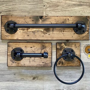 May include: A set of three rustic bathroom accessories made from reclaimed wood and black pipe fittings. The set includes a towel bar, a toilet paper holder, and a towel ring.