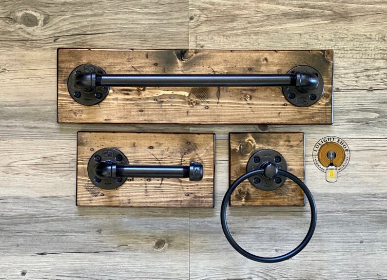 May include: A set of three rustic bathroom accessories made from reclaimed wood and black pipe fittings. The set includes a towel bar, a toilet paper holder, and a towel ring.