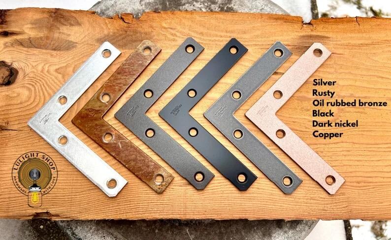 May include: Six metal corner brackets in different finishes: black, oil rubbed bronze, silver, dark nickel, and rusty.  The brackets are arranged in a row from left to right.