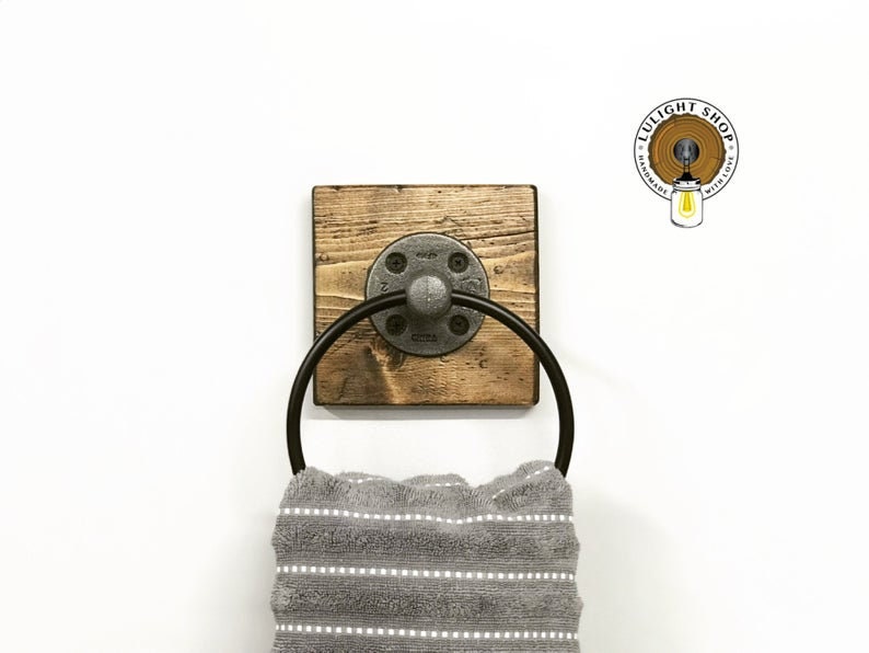 May include: A rustic wooden towel ring with a black metal ring and a pipe fitting. The ring is mounted on a white wall.