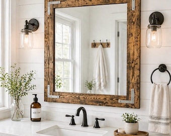 May include: A rectangular wall mirror with a dark stained wood frame featuring silver metal corner brackets. The mirror is mounted above a white bathroom vanity with a sink, black faucet, and two glass jar wall sconces on either side.