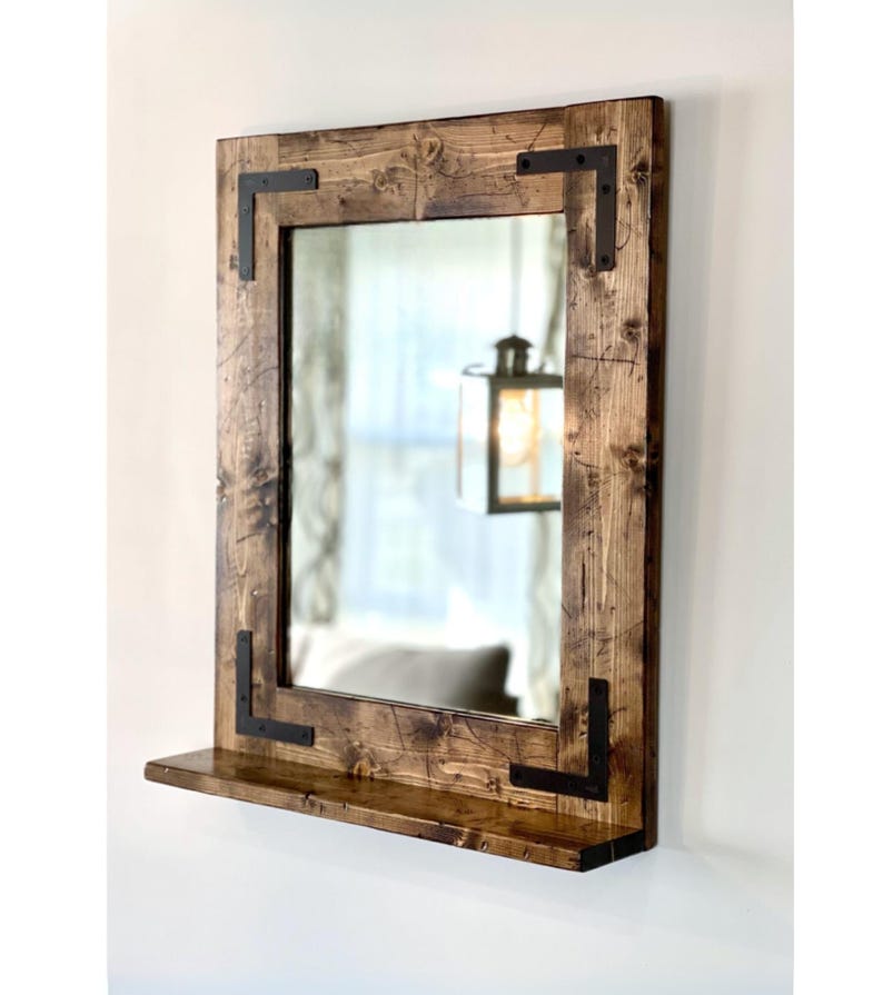 Handcrafted rustic wood framed mirror with a bottom shelf for storage, mounted on a bathroom vanity wall featuring a distressed finish and natural wood grain for a farmhouse-style charm.