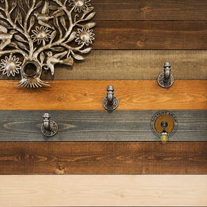 May include: A rustic wooden wall with three silver metal hooks. The wall is made of reclaimed wood planks in various shades of brown, gray, and white. A silver metal tree with flowers is mounted on the wall above the hooks. The text "LIGHT SHOP" is printed on a round sticker on the wall.