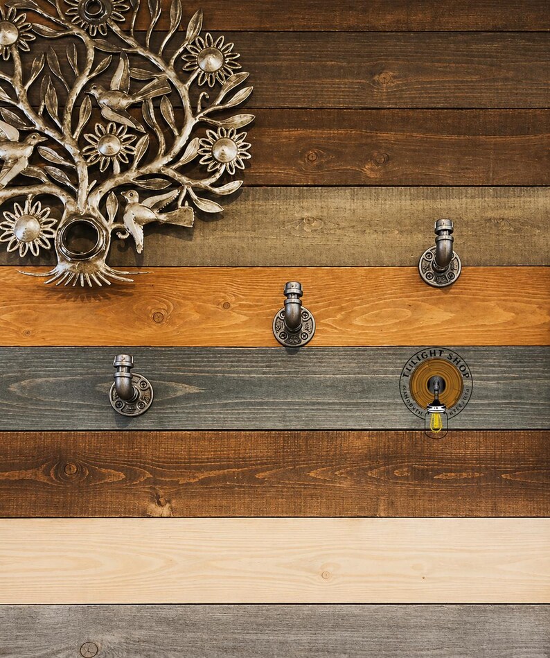 May include: A rustic wooden wall with three silver metal hooks. The wall is made of reclaimed wood planks in various shades of brown, gray, and white. A silver metal tree with flowers is mounted on the wall above the hooks. The text "LIGHT SHOP" is printed on a round sticker on the wall.