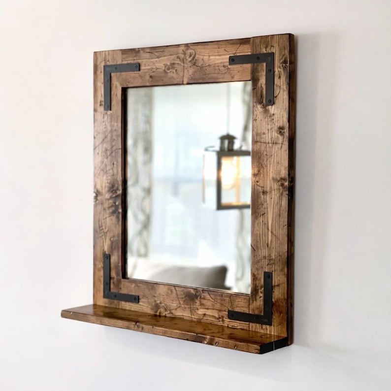 May include: A rustic wooden mirror with a rectangular frame and with a bottom shelf. The frame is made of reclaimed wood and has a dark brown stain. The mirror has a simple, modern design and would be a great addition to any home.