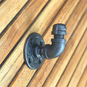 May include: A black metal pipe hook next to an entry for jackets, scarves, backpacks, hats hanging.