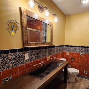 May include: A rustic bathroom with a wooden vanity and a large mirror. The vanity has a dark metal sink and copper faucets. The walls are decorated with patterned tiles in shades of red, black, and blue. Above the mirror are three vintage-style light fixtures.