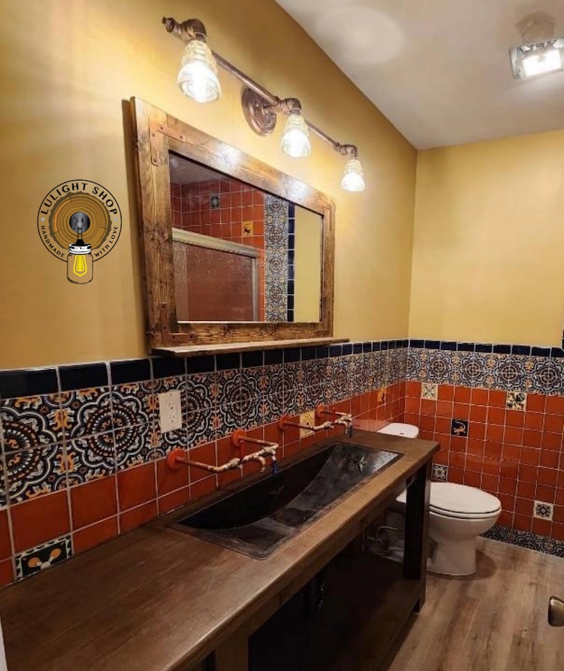 May include: A rustic bathroom with a wooden vanity and a large mirror. The vanity has a dark metal sink and copper faucets. The walls are decorated with patterned tiles in shades of red, black, and blue. Above the mirror are three vintage-style light fixtures.