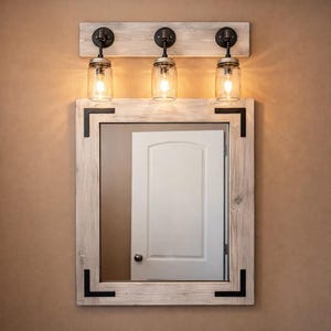 Handcrafted wood framed mirror mounted on a bathroom vanity wall with a three mason jar vanity light fixture on top, featuring a whitewash finish and natural wood grain for a farmhouse-style charm