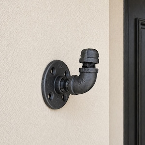 May include: A black metal pipe hook next to an entry for jackets, scarves, backpacks, hats hanging.