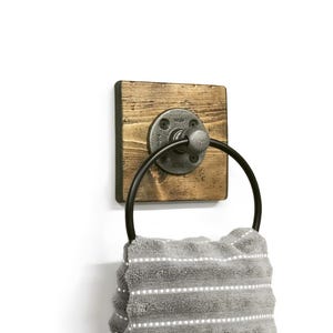 May include: A rustic wooden towel ring with a black metal ring and a gray metal pipe fitting. A gray and white striped towel is hanging on the ring.