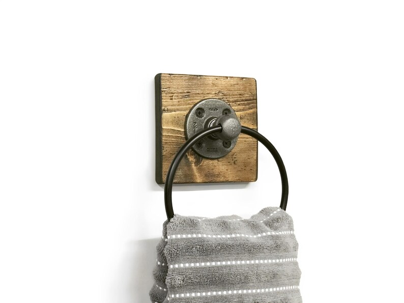 May include: A rustic wooden towel ring with a black metal ring and a gray metal pipe fitting. A gray and white striped towel is hanging on the ring.