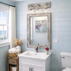 Handcrafted wood framed mirror mounted on a bathroom vanity wall with a three mason jar vanity light fixture on top, featuring a whitewash finish and natural wood grain for a farmhouse-style charm
