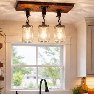 Farmhouse mason jar pendant light fixture with wood beam and chains hanging above rustic dining table in cozy kitchen