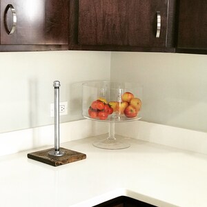 Puede incluir: Una encimera blanca con un cuenco de vidrio transparente lleno de tomates rojos y manzanas amarillas. Un toallero de tuber&iacute;a de plata con una base de madera est&aacute; en la encimera.