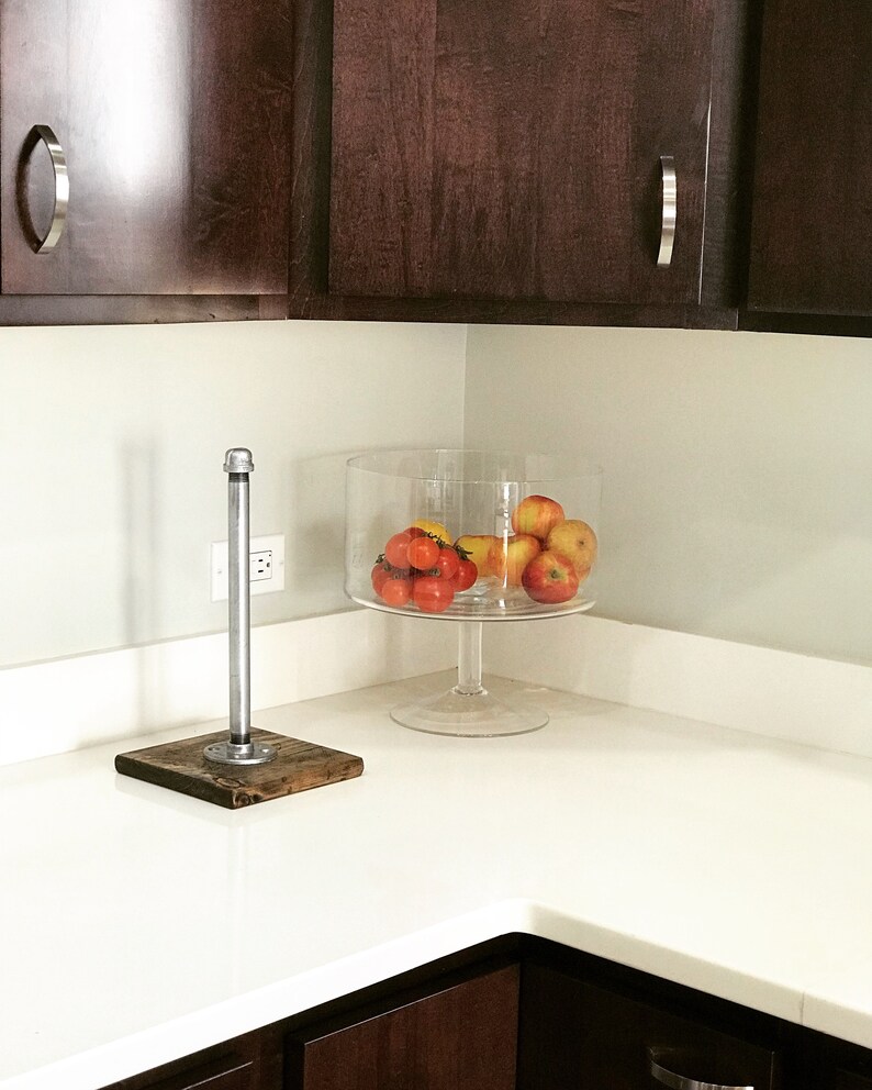 Puede incluir: Una encimera blanca con un cuenco de vidrio transparente lleno de tomates rojos y manzanas amarillas. Un toallero de tuber&iacute;a de plata con una base de madera est&aacute; en la encimera.
