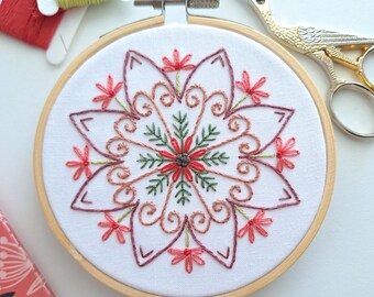 May include: A close-up of a finished embroidery hoop with a floral mandala design. The design features pink, red, and green thread on white fabric. The hoop is made of wood and has a natural finish. The text "PDF PATTERN" is printed below the hoop.