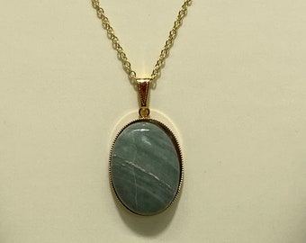 May include: A gold chain necklace with a green oval pendant. The pendant has a gold frame and a green stone with white veins.