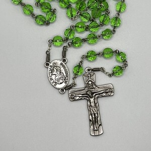 May include: A green glass rosary with a silver crucifix and a silver oval charm with the image of Saint Dominic.