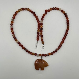 May include: A carnelian necklace with a carved carnelian bear pendant. The necklace is made of small, round beads in shades of red, orange, and brown.