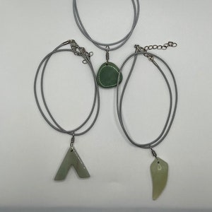 May include: Three necklaces with green stone pendants on gray cords. The pendants are different shapes: a teardrop, a triangle, and a rounded oval.
