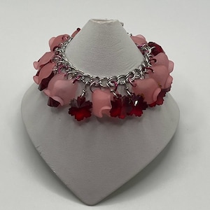 May include: A silver chain bracelet with pink and red flower-shaped charms. The charms are made of glass and have a frosted finish.