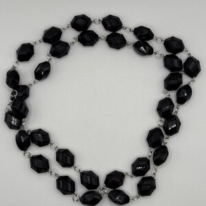 May include: A double-strand necklace featuring faceted black beads. The beads are connected by silver-toned chain links. The necklace is displayed against a white background, highlighting the contrast between the dark beads and the bright backdrop.