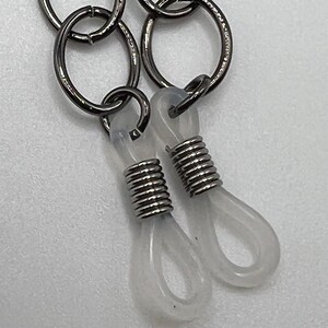 May include: A close-up of a black metal chain with two clear plastic loops attached to the end. The loops have a spring coil inside.