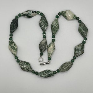 May include: A green and white agate gemstone necklace with a silver clasp. The necklace is made of faceted, diamond-shaped beads.