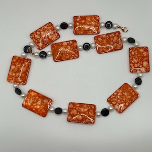 May include: A necklace with orange and white rectangular beads and black round beads.